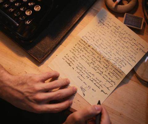 Hands writing a letter. A typewriter is nearby.