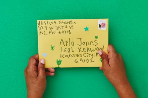 Child's hands holding a letter, addressed in childlike handwriting with small doodles on the envelope