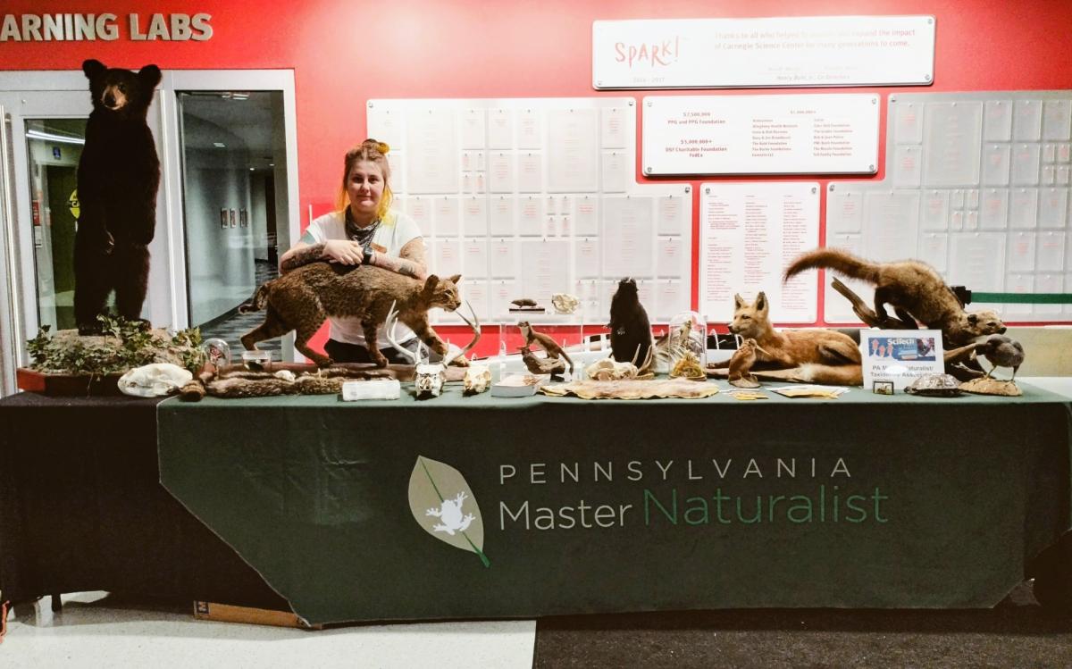 An image of presentewr Char Ross with a table of taxidermied animals. PA MAster Naturalist Tablecloth is in the foreground.