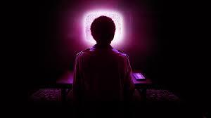 An image of someone sitting in front of a tv screen, bathed in its purple light.